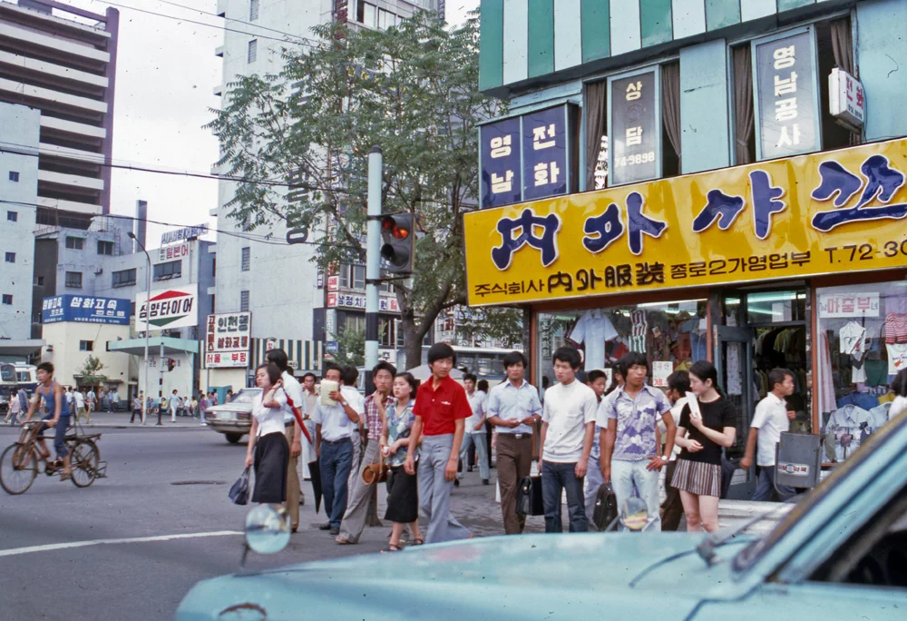 시민들이 서 있는 뒤편으로 '내외(內外)샤쓰' 종로2가 영업부의 노란색 간판이 보인다. 내외샤쓰는 1970년대 중반까지 세계 15개국에 수출하고 전국 300개 이상의 체인점을 두며 인기를 끌었고, 사진이 촬영된 1년 후인 1976년 6월에 부산제복(釜山制服)과 합병하며 사세를 키웠다. 1